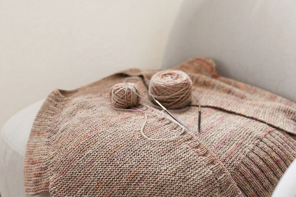 Eine kraus rechts gestrickte Jacke mit Stricknadeln und Wolle liegt auf einem Hocker
