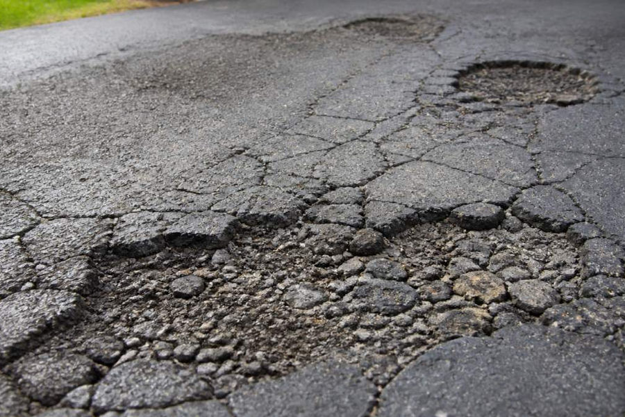 Close-up of deteriorated asphalt driveway showing visible cracks, surface raveling, and potholes with weather-worn edges and exposed base layer