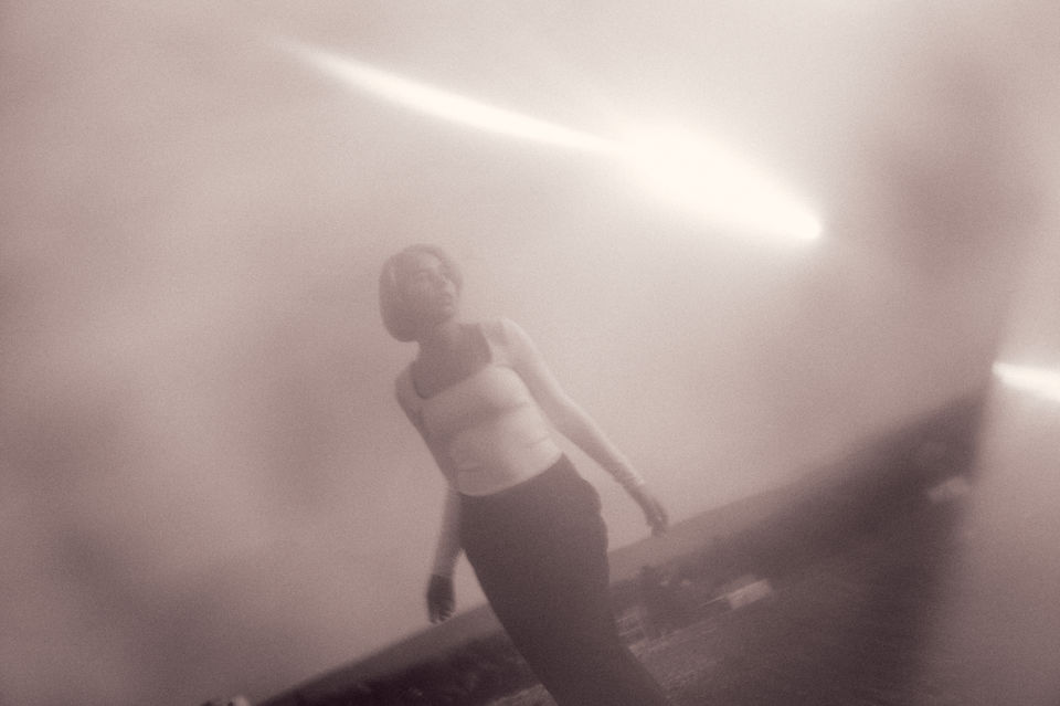 Girl on a rooftop looking at a light beam crossing the image.