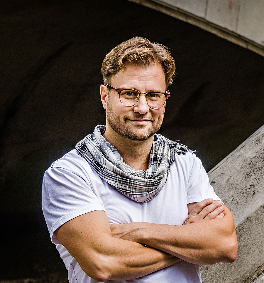 Man with glasses and scarf standing with arms crossed