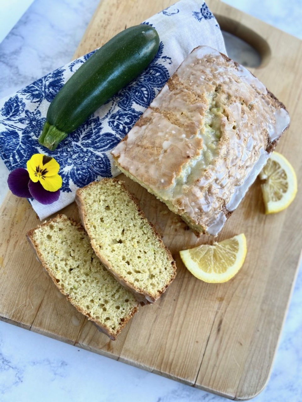 Lemon zucchini loaf from above. Two slices of loaf in front. Lemon wedges on the side.
