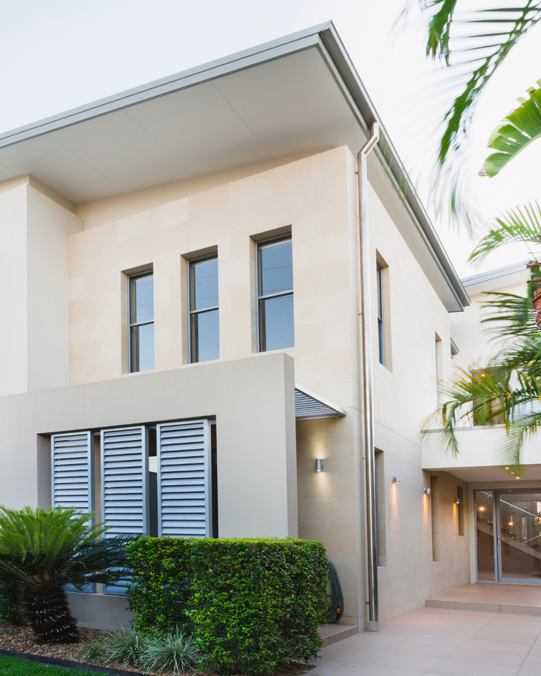 Modern beige house exterior with multiple windows and tropical landscaping.