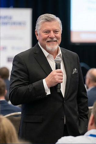 Ron with mic and black jacket.png