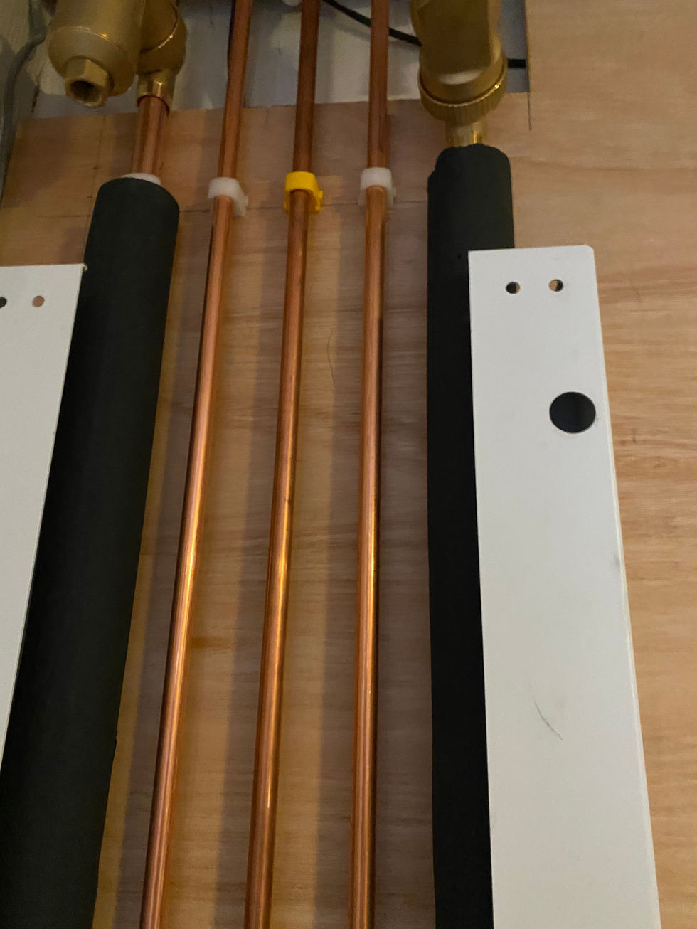 copper pipes are lined up on a wooden wall