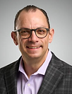 Smiling man with glasses in a plaid blazer and lavender shirt