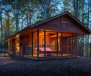Modern wooden cabin with screened porch in a forest.