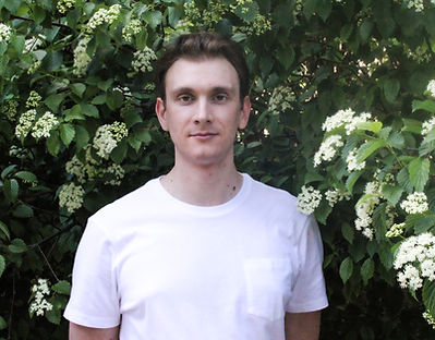 Drew Comer, Bass standing in front of a floral bush in a white tee