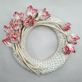 White ceramic wreath adorned with white and red tipped tulips gathered on the top left and a few reaching over the top right side of the wreath.