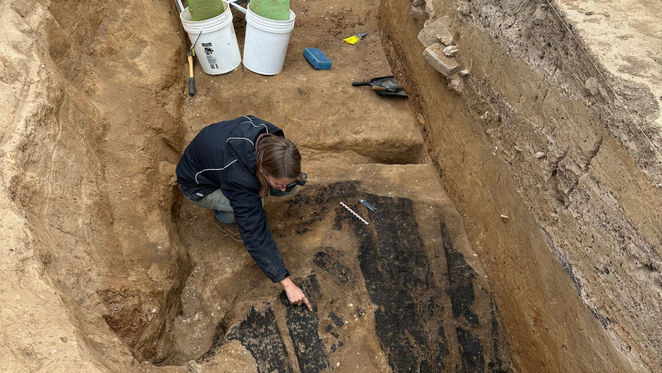 Archaeologist in the bottom of a pit pointing to charred wood