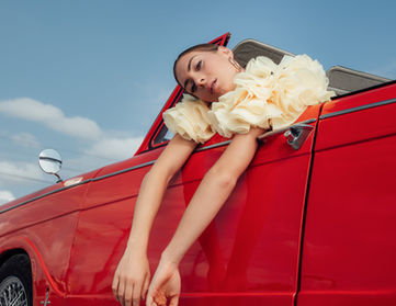 Woman leaning on the door of a red vintage car, fashion photo shoot in Paris