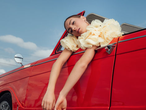 Woman leaning on the door of a red vintage car, fashion photo shoot in Paris