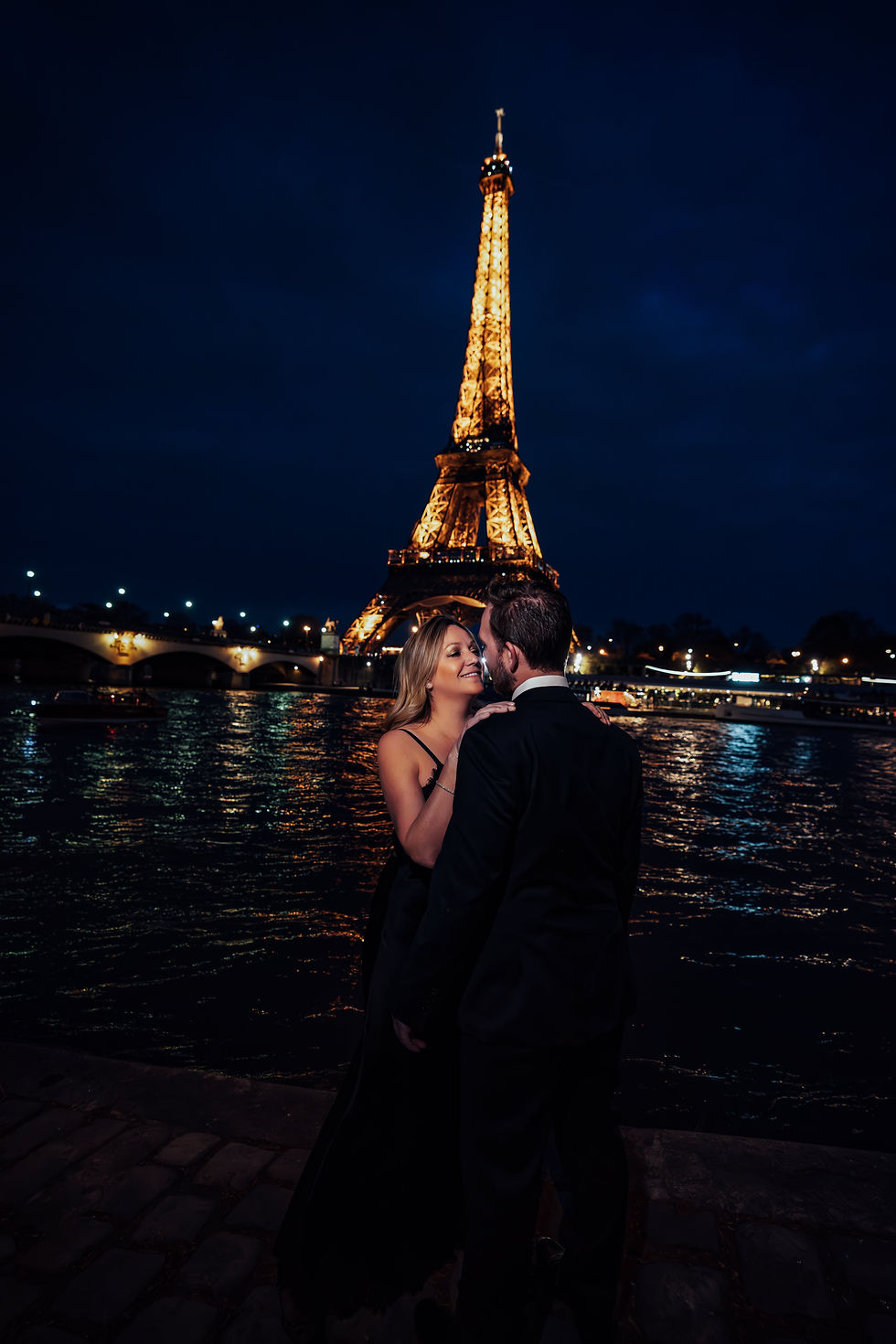 Couple embracing at night by the Seine in front of the illuminated Eiffel Tower