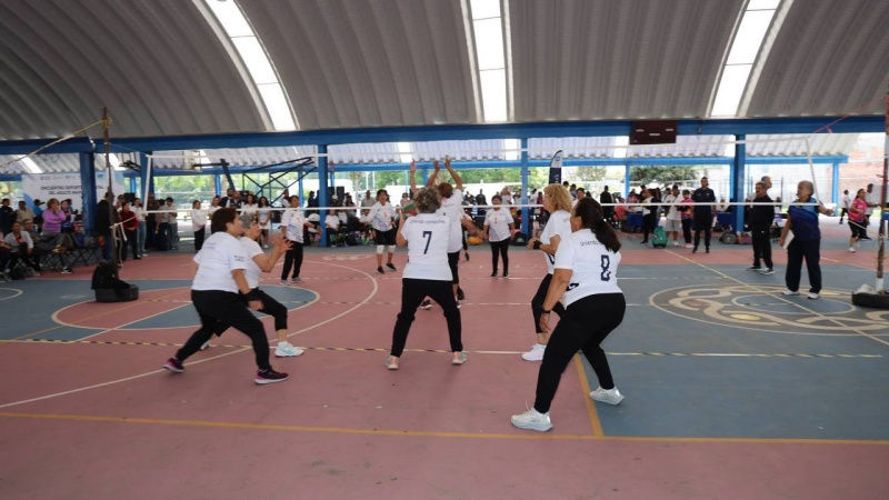 Personas mayores participan en un partido de voleibol bajo techo, destacando la importancia de la actividad física para una mejor calidad de vida en la vejez.