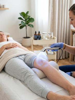 Um consultório terapêutico com uma pessoa deitada numa maca e o terapeuta aplicando terapia Plasmática em seu joelho.