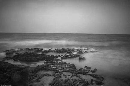 Rocky shoreline with misty waves in black and white.