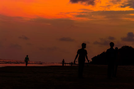 Silhouetted figures on beach at sunset.