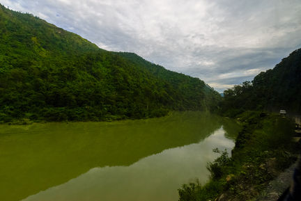 River surrounded by lush green hills under cloudy sky.
