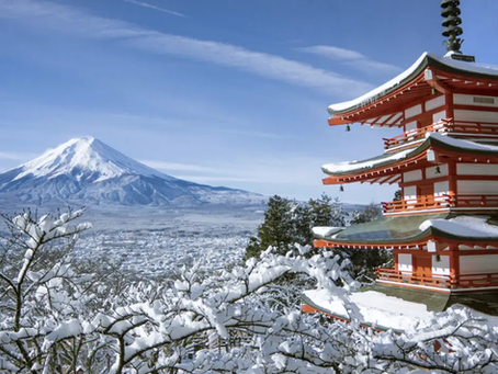 Snow-covered Mount Fuji under a clear blue sky with a red pagoda in the foreground. Snow-laden trees add a serene winter mood.