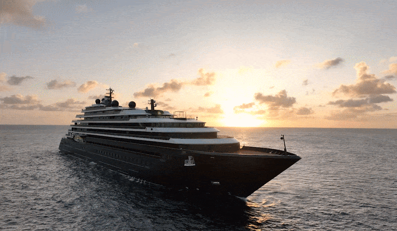 Luxury yacht sailing at sunset on open sea. The sky is filled with soft clouds and the sun creates a warm, serene glow over the water.
