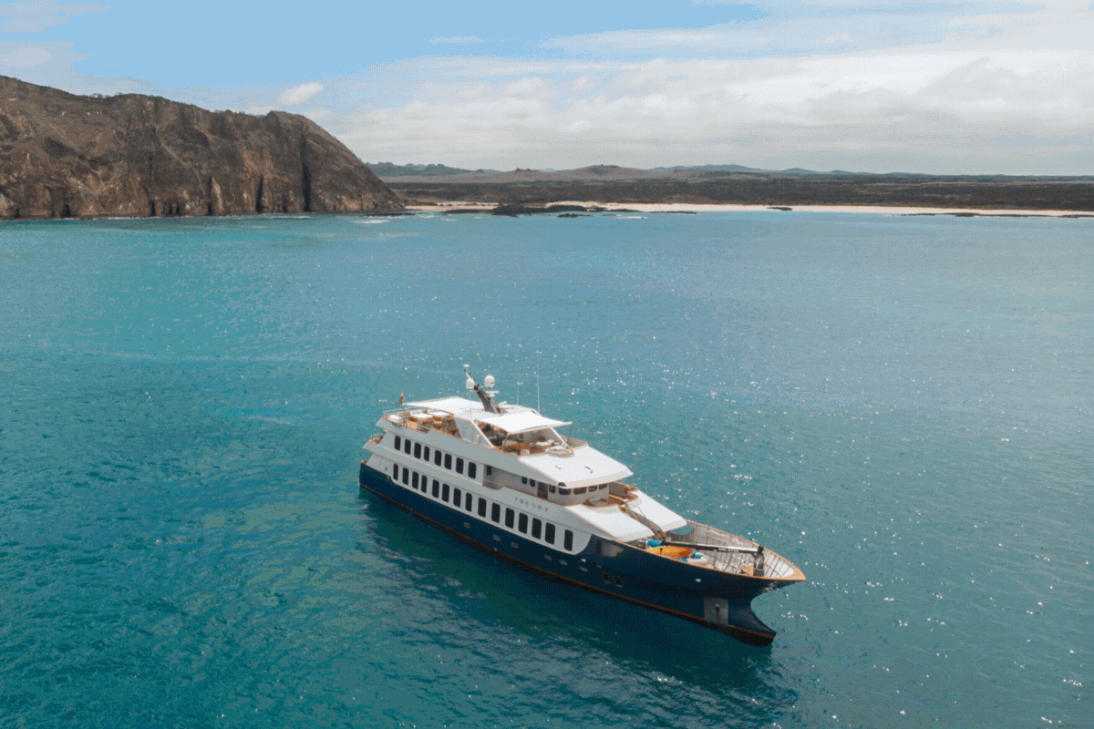 Luxury yacht on clear turquoise waters near rocky coastline under a partly cloudy sky, conveying a serene and adventurous mood.