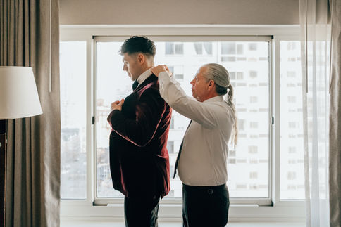 Person adjusting another's suit in a bright room.