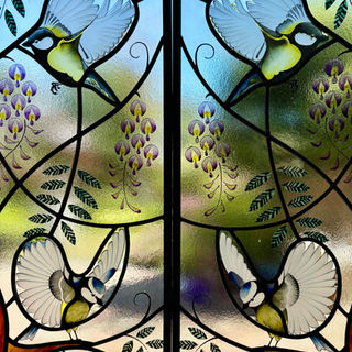Detail of painted and sandblasted birds; Great Tits and Blue Tits, for 2 front door lights. Birds have wings spread and are depicted amongst trailing wisteria vines, leaves and flowers. Hand made by Seaview Studio, Hampshire