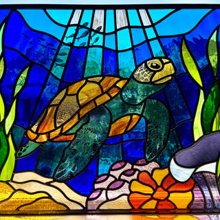 Vibrant and fun underwater scene bathroom window, depicting a sea turtle detailed with traditional glass paint work. The graduated colour in the water, kelp and coral all help to give the design depth and movement. Made using traditional leadwork by Seaview Studio, Hampshire.
