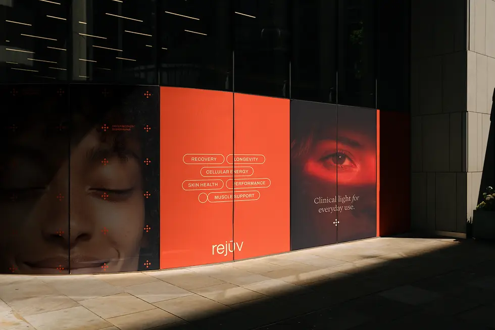 A large outdoor Rejuv brand hoarding on a city street, featuring a smiling face with orange markers, pill-shaped benefit labels including recovery, skin health and muscle support, and the tagline "Clinical light for everyday use."