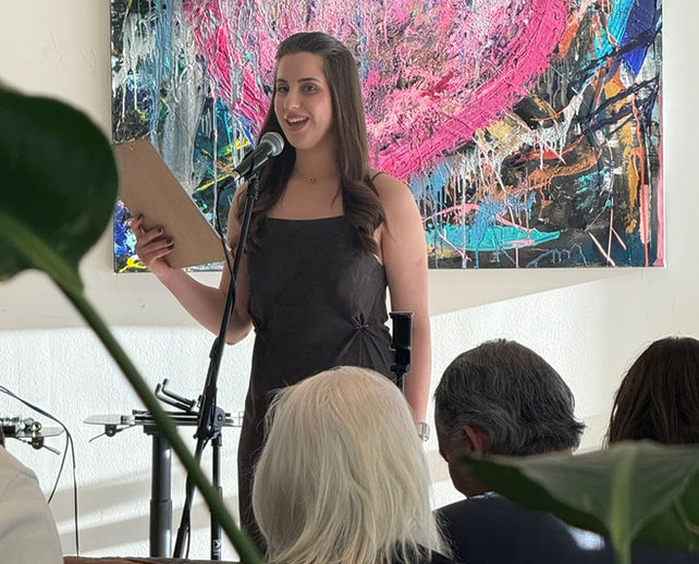 Emcee, Yuliia Kovalenko. A woman standing at a microphone and speaking to the audience. Abstract art is in the background.