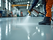 A worker spraying industrial resin onto a large floor area in a factory setting, highlight