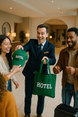 Hotel staff member smiling and handing custom branded green tote bag and cap with "HOTEL" printed on them to happy guests at check-in.