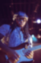 Leon Thomas performing live in Vancouver with his guitar during the Mutts Don’t Heel Tour, captured in an intense close-up shot wearing a metallic vest and leather beret, exuding confidence under golden stage lights.