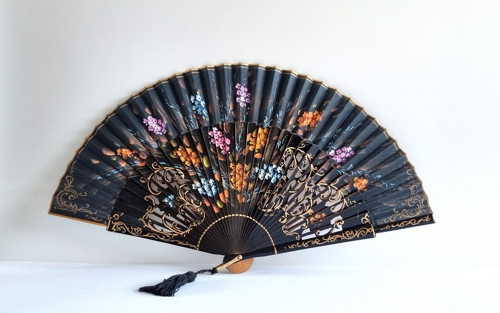 Schwarzer Vintage‑Fächer mit floraler Handbemalung in Blau, Lila, Rosa und Erdtönen.
