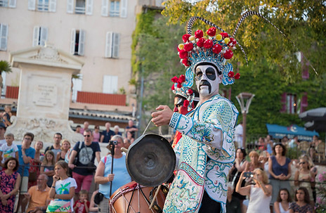 Artiste maquillé et costumé dans la tradition chinoise, jouant du gong au cœur d’une foule lors d’une performance de rue