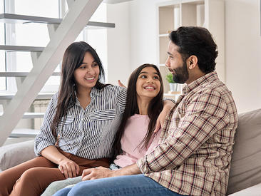 South Asian family sits on a couch smiling