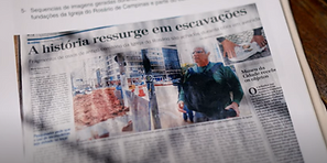 Frame do filme Escombros. Detalhe de um recorte de jornal. Ao centro, numa diagonal suave, fotografia jornalística de um senhor em via pública. Tem cabelos brancos e veste camiseta de manga longa verde. Tem a mochila pendurada nos ombros junto à parte frontal do corpo. Na parte superior vista parcial da manchete “essurge em escavaç”.
