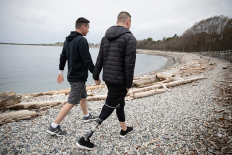 Two men dressed warmly walking hand in hand along a rocky shoreline