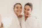 happy-caucasian-women-use-eye-patches-wear-bathrobes-look-camera-white-background-concept-