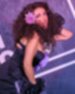 Drag performer with dramatic makeup, big hair, and purple flower