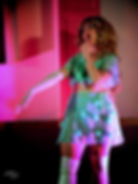 Performer in a teal outfit, posing suggestively under pink lights