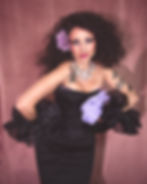 Woman in black strapless dress, curly hair, purple flower, tattoos.