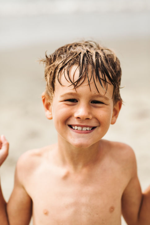 a portrait of a boy smiling at the camera on a beach.