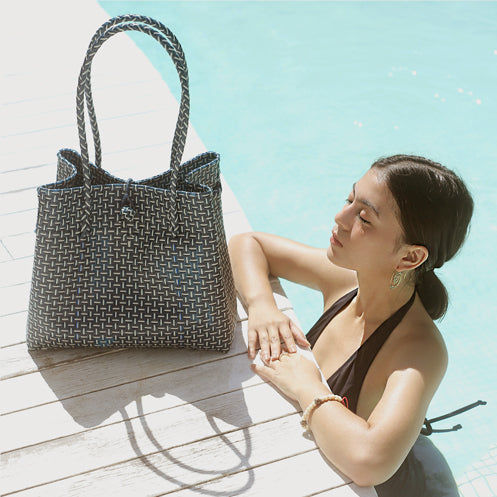 Woman in black swimsuit by pool with handbag