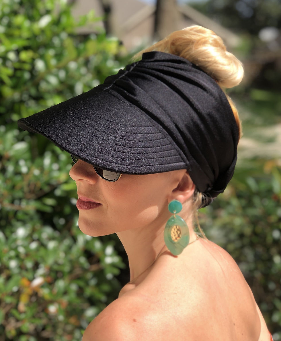 Woman wearing black sun visor, sunglasses, and green earrings