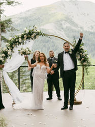 Bride and groom celebrating at the altar at Noble Ridge Tree Deck, framed by a circular floral arch, surrounded by cheering wedding party and lush mountain views of the Pacific Northwest.