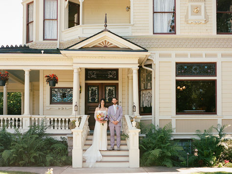 Bride and groom posing for a photo on the steps of the Victorian Belle house.
