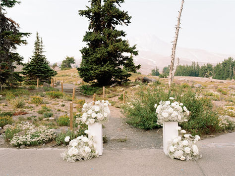 A gorgeous ceremony altar set up with white pillars both topped and surrounded by large white floral arrangements with the peak of Mt. hood slightly visible through the fog.