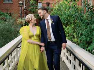 Bride in a fun chartreuse dress walking arm in arm with her groom, sharing a loving glance, down a fenced path surrounded by greenery.