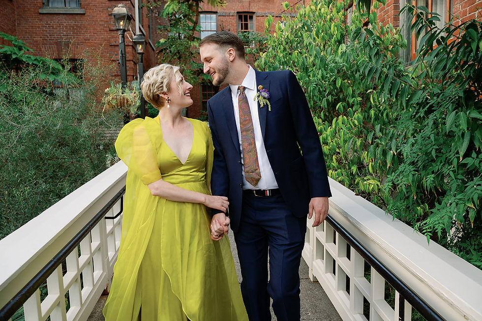 Bride in a fun chartreuse dress walking arm in arm with her groom, sharing a loving glance, down a fenced path surrounded by greenery.