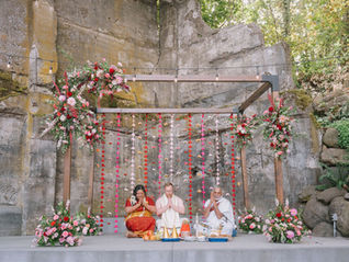 Bride and groom sitting under a Mandap, participating in a colorful Indian wedding ceremony.